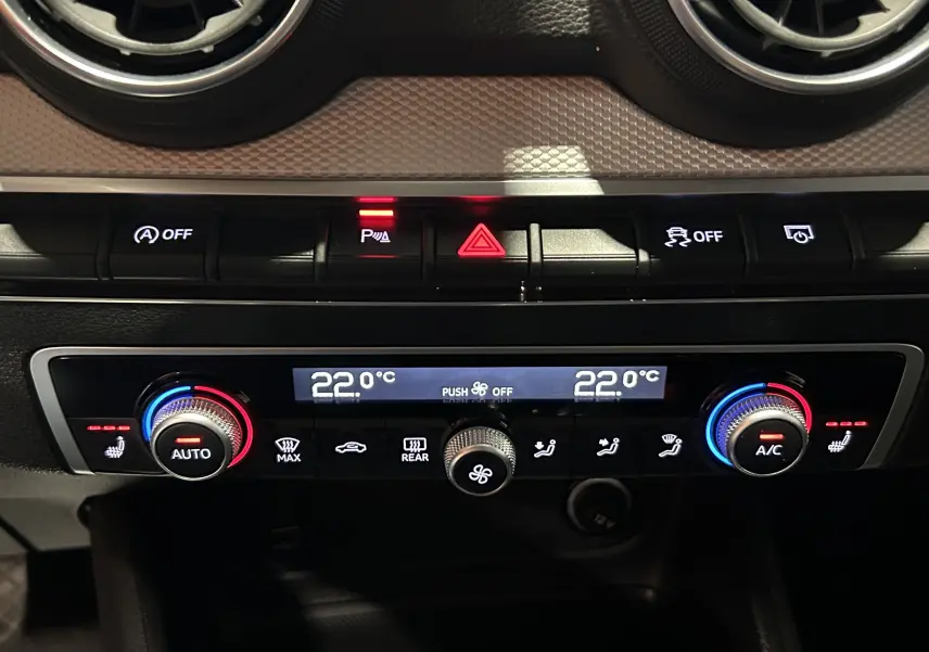 Gros plan sur le bouton de réglage de la climatisation et siège chauffant dans l'Audi Q2 noir métal 2023.