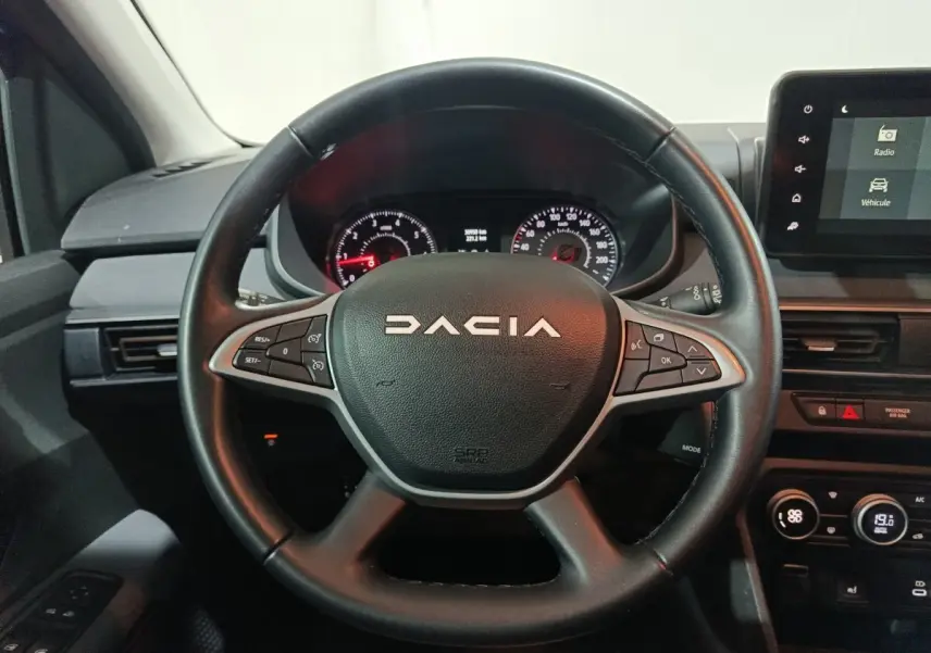 Vue centrée sur le volant en cuir noir de la Dacia Sandero 2024 avec tableau de bord et écran tactile à droite.