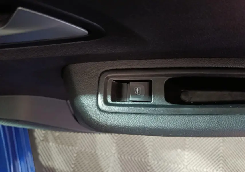 Gros plan sur le bouton de commande de la vitre électrique côté conducteur, avec partie de la porte bleu visible.
