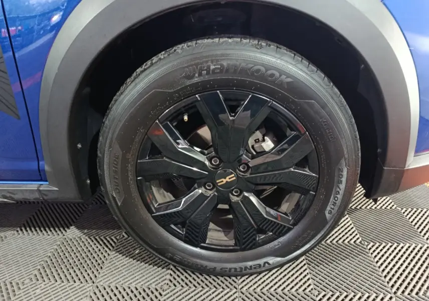 Gros plan sur la roue avant droite noire brillante d'une Dacia Sandero Extreme+ bleu 2024 avec jante design.