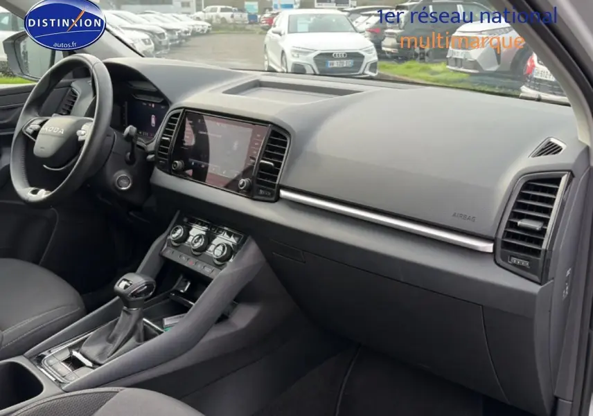 Vue intérieure côté passager du tableau de bord et console centrale du Skoda Karoq blanc glacial, avec écran tactile et volant cuir multifonction.