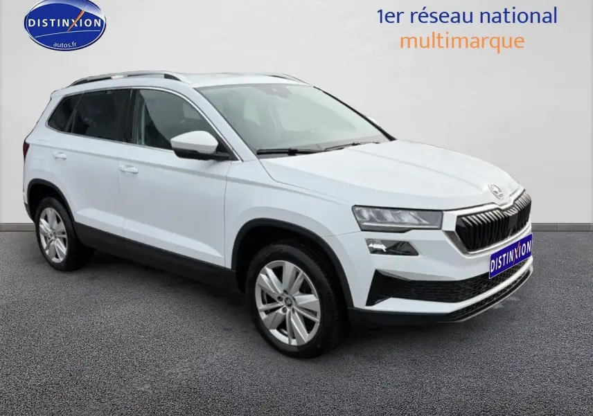 Vue 3/4 avant d'un Skoda Karoq blanc glacial avec jantes alu et barres de toit noires sur fond neutre.