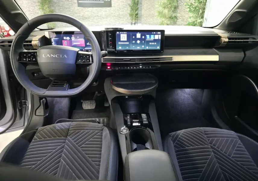 Vue intérieure avant de la Lancia Ypsilon 2025, avec tableau de bord digital et sellerie velours gris anthracite.