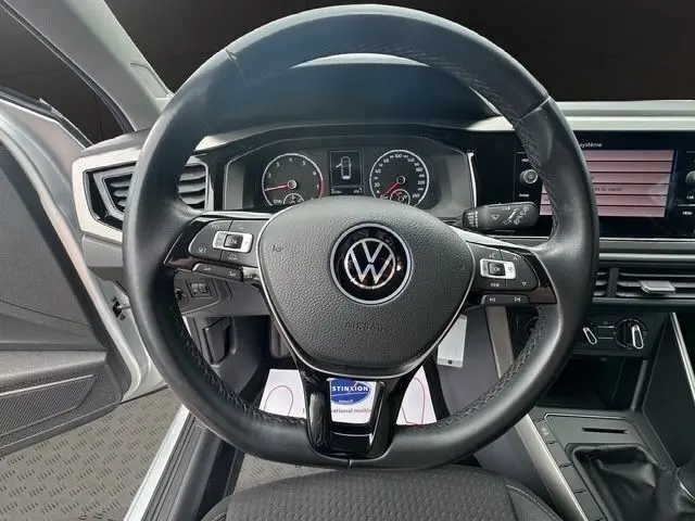 Vue rapprochée du volant cuir et alu multifonctions d’une Volkswagen Polo gris clair, avec tableau de bord numérique visible.