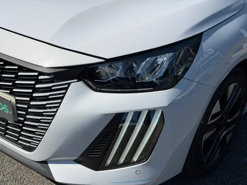 Gros plan sur l'avant droit de la Peugeot 208 blanche Okénite, mettant en valeur les phares LED et la calandre distinctive.