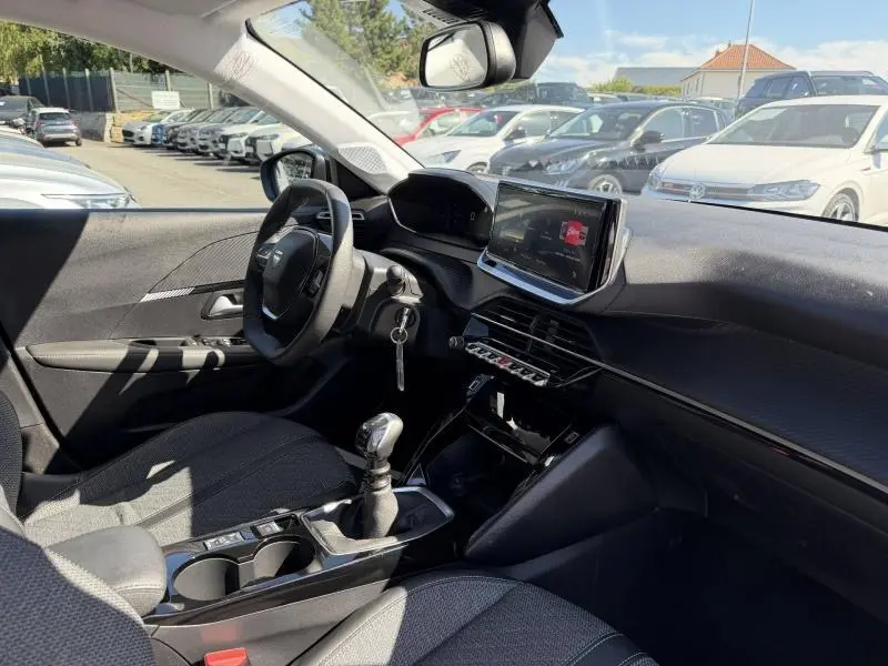 Intérieur de la Peugeot 208 blanc Okénite, vue côté conducteur montrant volant, écran tactile et levier de vitesse manuel.