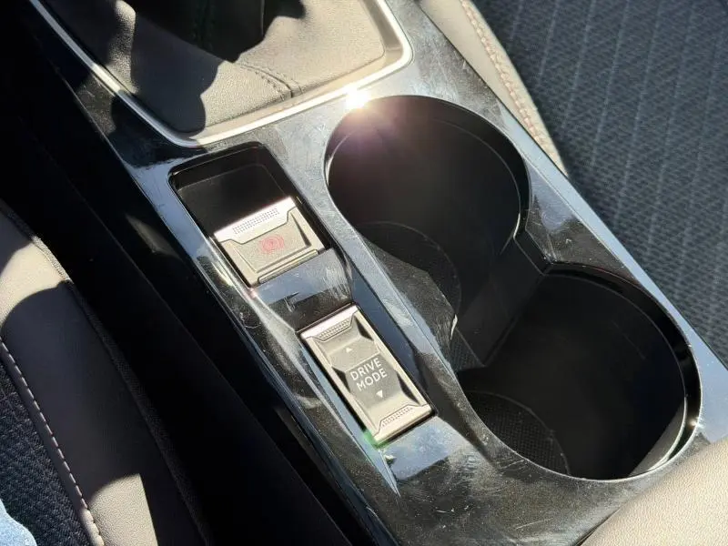 Gros plan sur la console centrale noire brillante de la Peugeot 208 2025 avec commandes frein à main et mode de conduite.