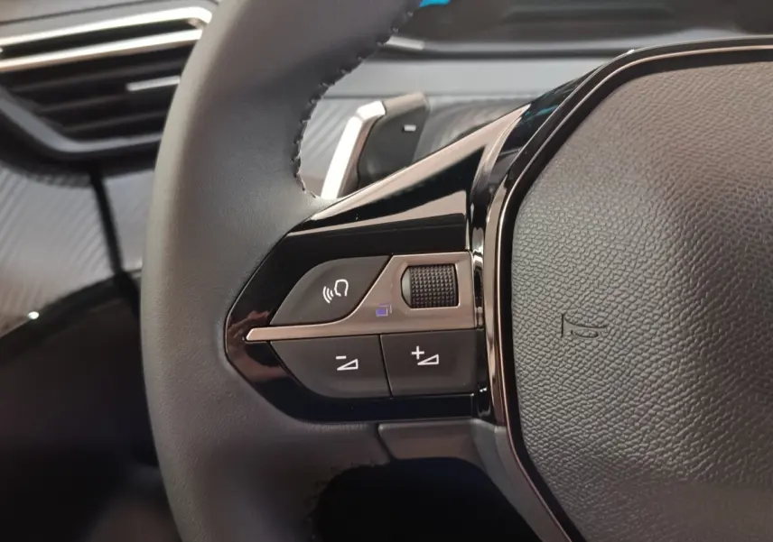 Gros plan sur le volant cuir multifonctions de la Peugeot 208 Hybrid 100 e-DCS6 Style, avec commandes audio intégrées.