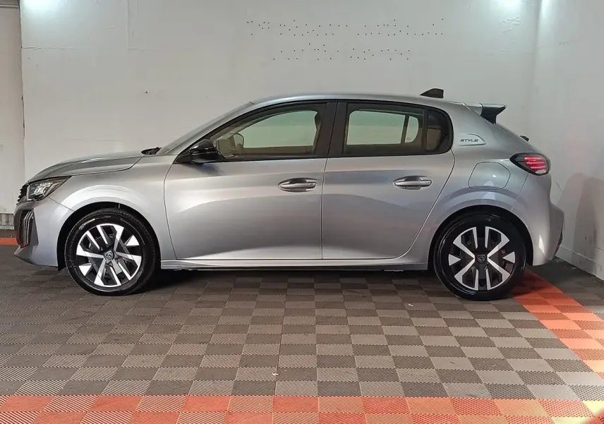 Profil droit de la Peugeot 208 Hybrid gris clair 2025 avec jantes stylisées et badge Style sur l'aile arrière.