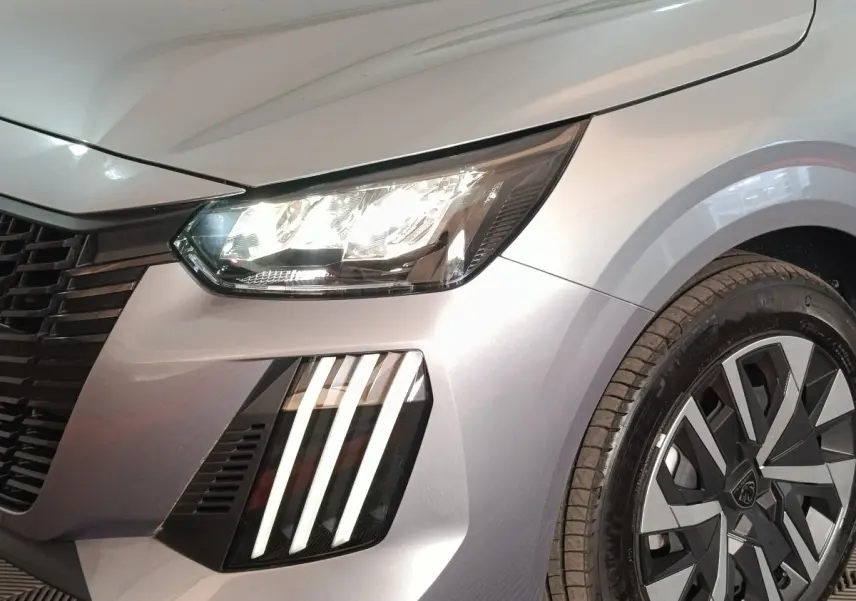 Gros plan sur l'avant droit gris clair de la Peugeot 208 Hybrid 100 avec phares LED et jante au design moderne.