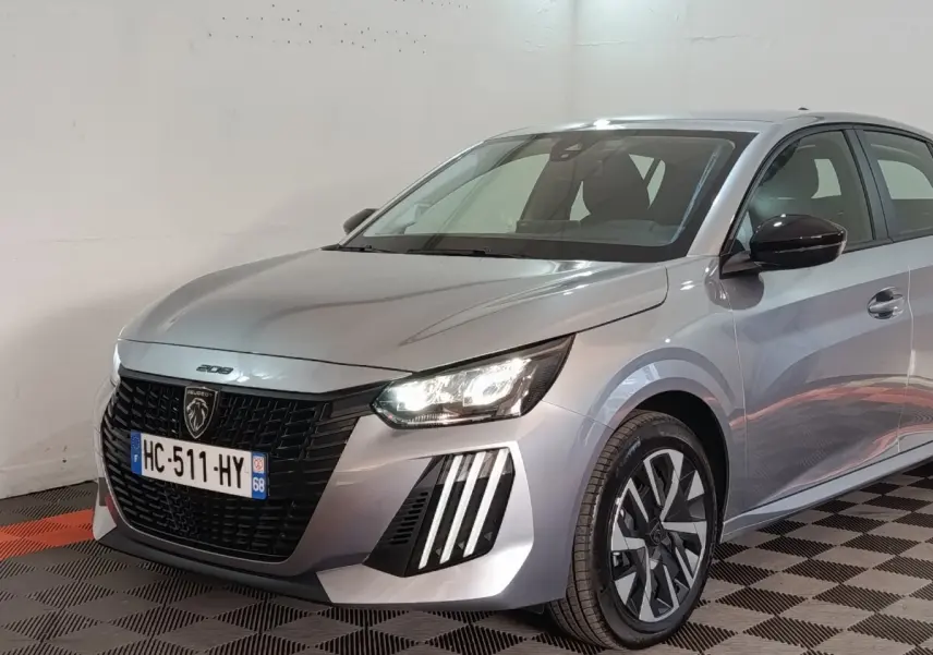 Vue 3/4 avant droit d'une Peugeot 208 Hybrid gris clair avec phares LED et calandre noire distinctive.