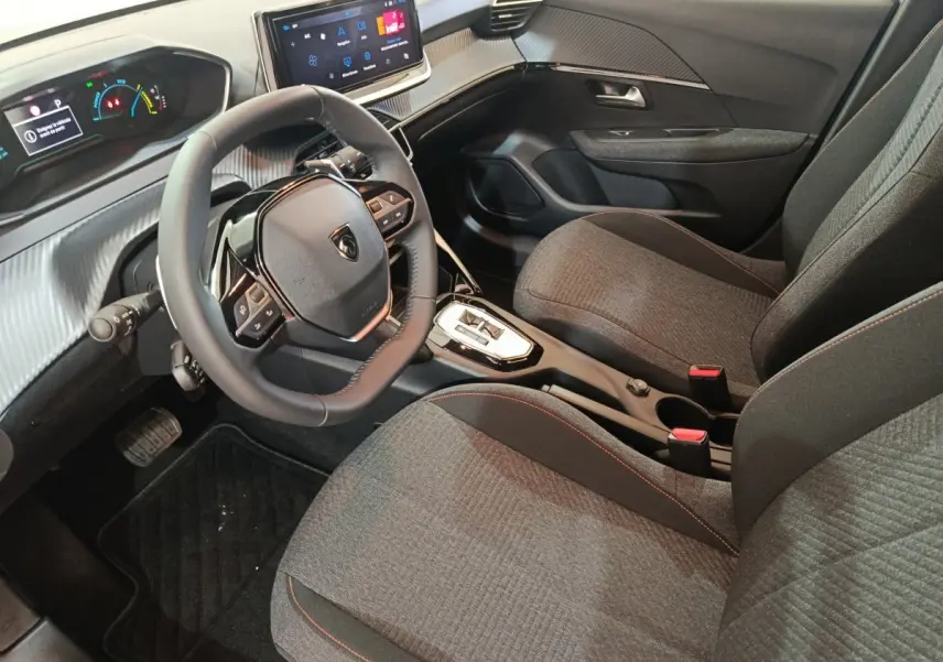 Vue intérieure côté conducteur de la Peugeot 208 Hybrid 100 e-DCS6 Style 2025, sièges gris et volant cuir multifonctions.
