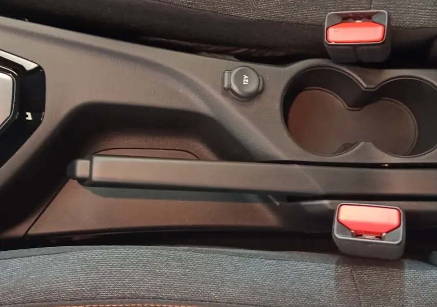 Gros plan sur la console centrale noire de la Peugeot 208 Hybrid 2025, montrant frein à main, prise 12V et porte-gobelets.