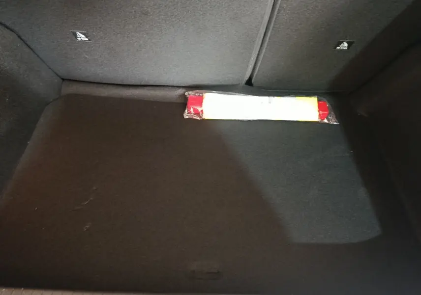 Coffre vide de Peugeot 208 Hybrid gris clair, vue intérieure montrant la moquette noire et un triangle de signalisation.