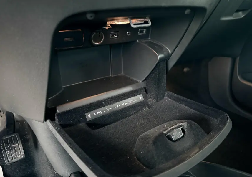 Intérieur de la Citroën C4 Picasso 2015, vue sur le rangement sous le tableau de bord côté conducteur avec prises USB et allume-cigare.