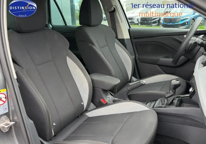 Vue intérieure côté avant gauche du Skoda Kamiq gris 2025, sièges tissu bicolore avec accoudoir central.