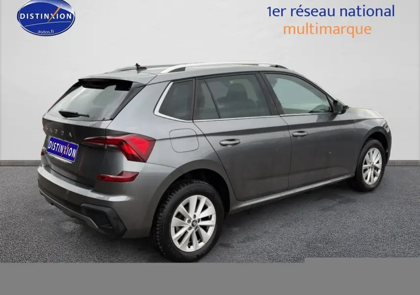 Vue 3/4 arrière droite d'un Skoda Kamiq gris 2025 avec barres de toit et jantes alu visibles.
