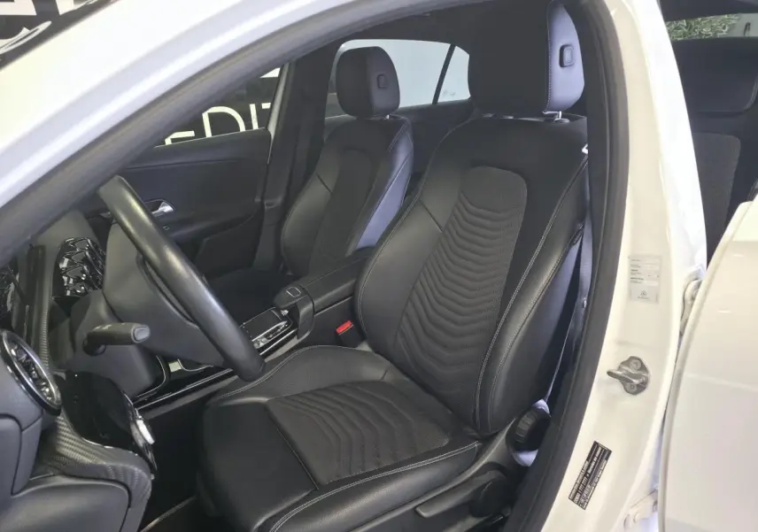 Vue intérieure côté conducteur d'une Mercedes Classe A blanche 2019, sièges sport noirs en tissu et similicuir.