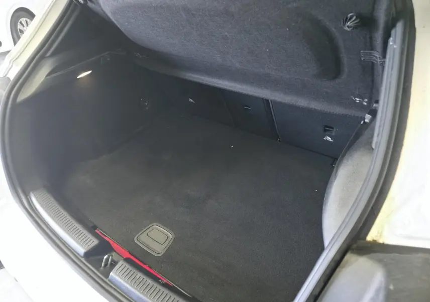 Coffre ouvert vu de dessus d'une Mercedes Classe A blanche, montrant la moquette noire et l'éclairage intérieur.