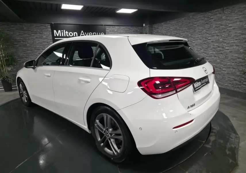 Vue 3/4 arrière droite d'une Mercedes Classe A 160 blanche avec jantes alliage gris Himalaya dans un showroom.