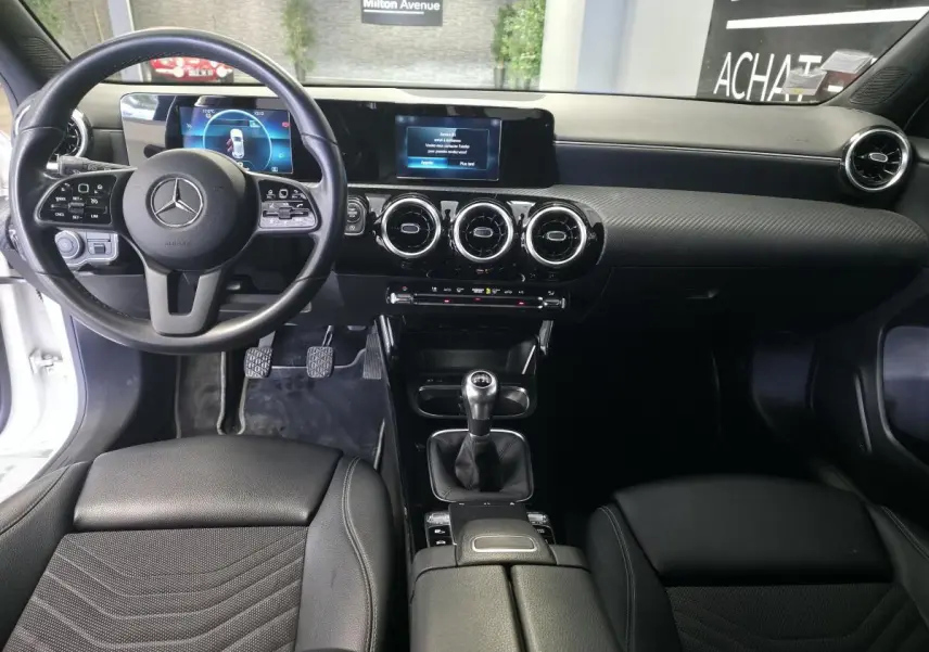 Vue intérieure avant de la Mercedes Classe A 160 Style Line 2019, volant cuir, tableau de bord numérique et levier de vitesse manuel.