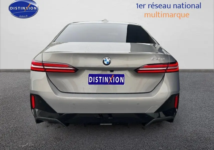 Vue arrière d'une BMW Série 5 gris clair (520da M Sport) avec feux LED et logo distinctif au centre.