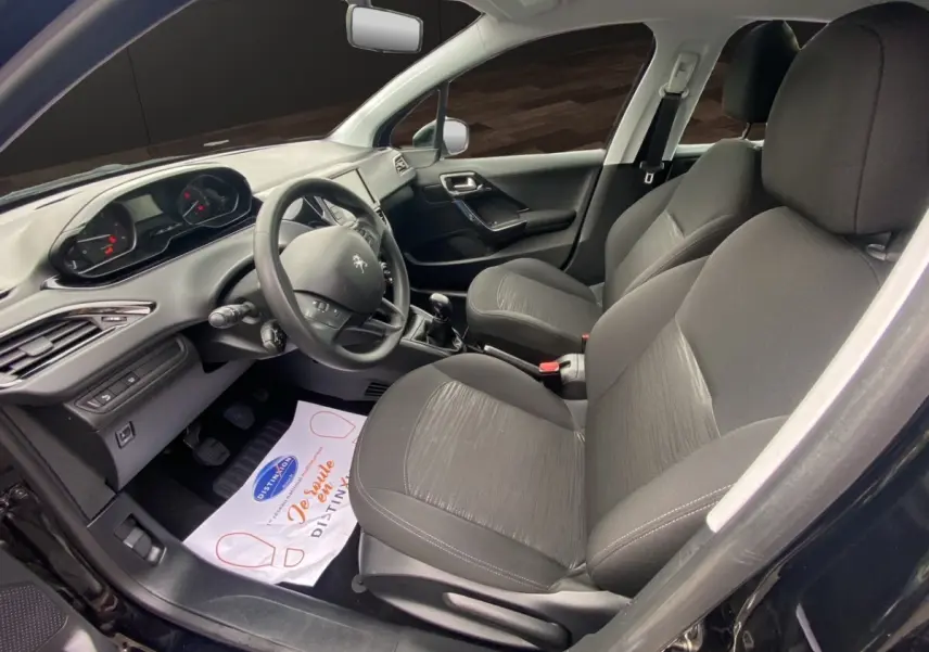 Vue intérieure côté conducteur de la Peugeot 208 Affaire noire, montrant le volant, tableau de bord et sièges tissu gris.