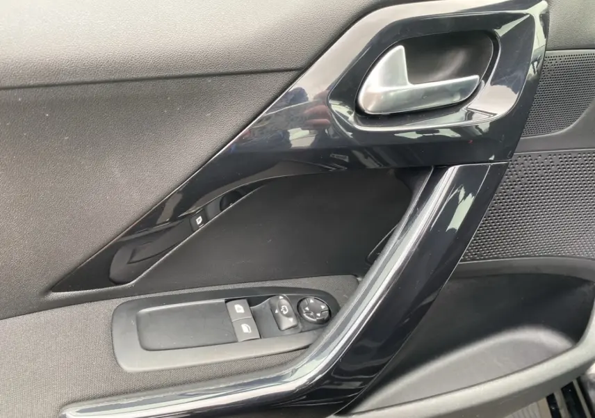 Vue rapprochée de la porte côté conducteur noire de la Peugeot 208 AFFAIRE avec commandes électriques des vitres et poignée brillante.