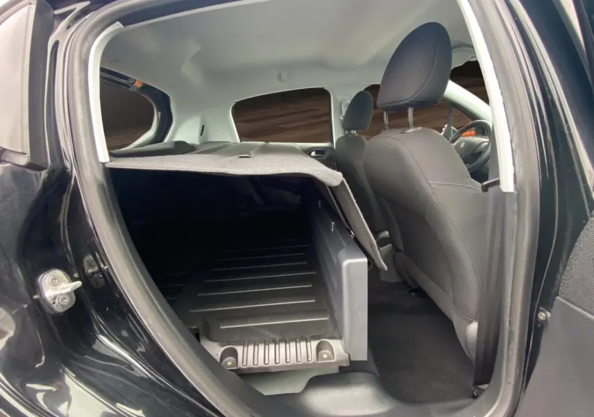 Vue intérieure côté droit de la Peugeot 208 Affaire noire, montrant l'espace de chargement avec cloison partielle et sièges avant.