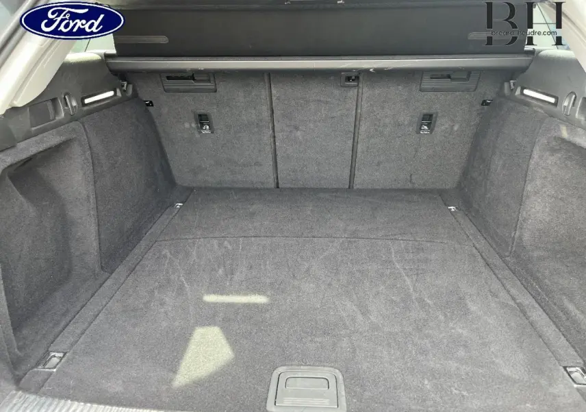 Coffre spacieux vu de l'arrière, tapis gris foncé, avec cache-bagages et fixations Isofix visibles.