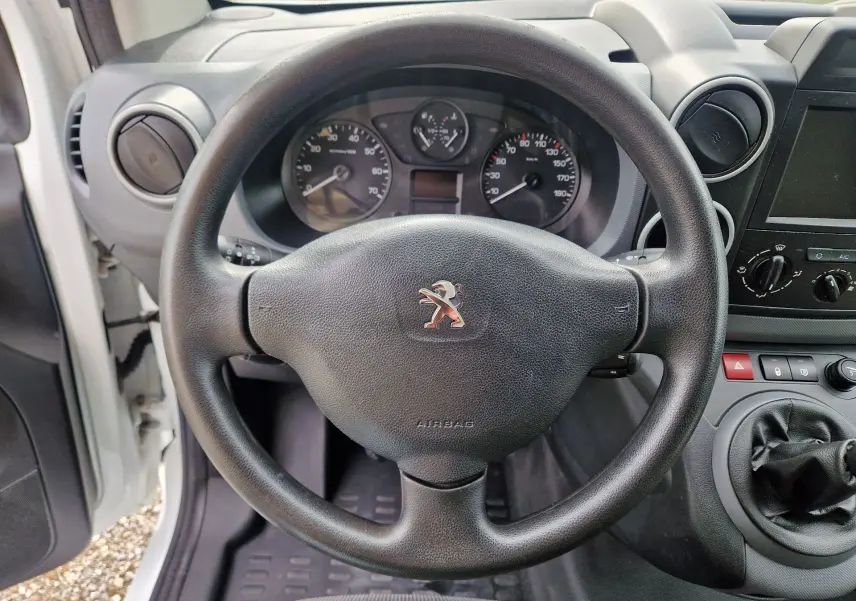 Vue rapprochée du volant noir et du tableau de bord du Peugeot Partner blanc, avec levier de vitesses manuel visible.
