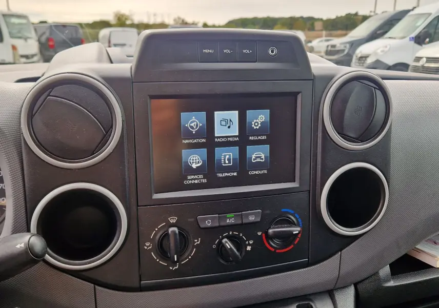 Vue rapprochée du tableau de bord du Peugeot Partner blanc, mettant en valeur l’écran tactile et les commandes de climatisation.