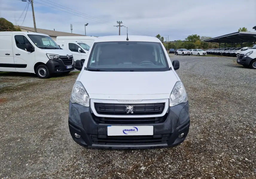 Vue de face d’un Peugeot Partner blanc de 2017 avec pare-chocs avant noir et calandre distinctive sur un terrain gravillonné.