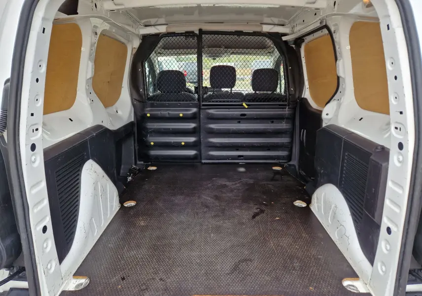 Vue intérieure arrière du Peugeot Partner blanc 2017, montrant l’espace de chargement avec cloison grillagée et panneaux bois latéraux.