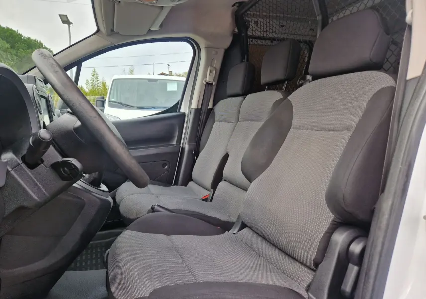 Intérieur côté gauche du Peugeot Partner blanc 2017, montrant les sièges avant gris et la grille de séparation derrière.