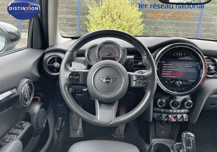 Vue intérieure centrée sur le volant et le tableau de bord d'une MINI 1.5 136CH STEPTRONIC noire, avec écran tactile rond.