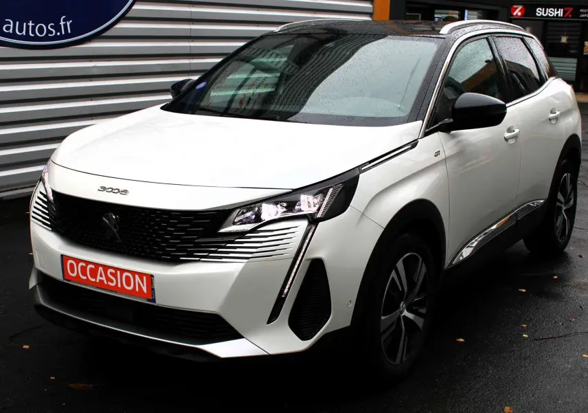 Peugeot 3008 blanc nacré en 3/4 avant droit, avec toit panoramique noir et feux LED allumés sur sol humide.