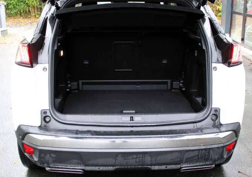 Vue arrière du Peugeot 3008 blanc nacré 2025 avec coffre ouvert et feux arrière allumés.