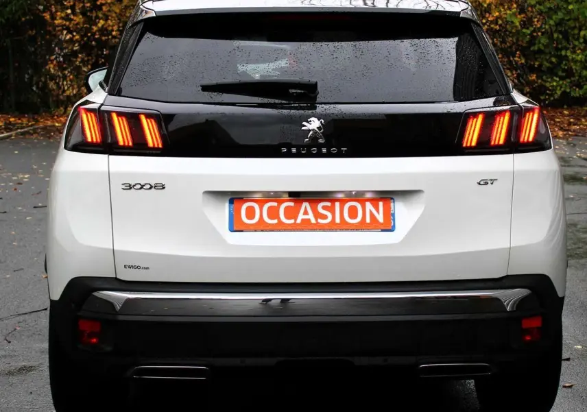 Vue arrière d'un Peugeot 3008 blanc nacré avec feux allumés et toit panoramique ouvrant visible.