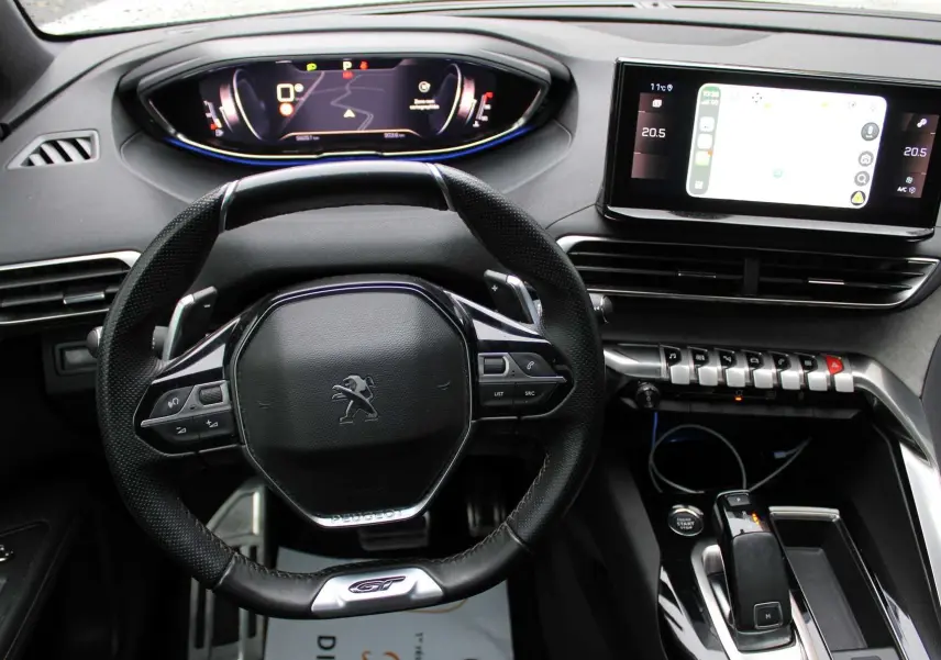 Vue rapprochée de l’intérieur du Peugeot 3008 2025, volant GT noir et tableau de bord digital avec écran tactile central.