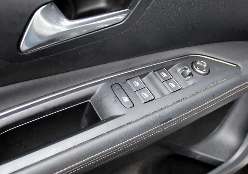 Gros plan sur la commande des vitres et rétroviseurs côté gauche d'une Peugeot 3008 2025 finition GT noire.