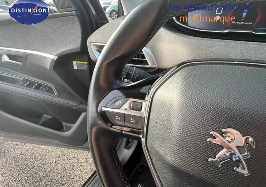Vue intérieure côté conducteur du Peugeot 5008 noir, mettant en valeur le volant cuir avec commandes intégrées et la porte ouverte.