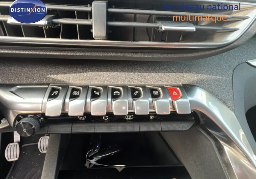 Gros plan sur la rangée de boutons argentés et rouges du tableau de bord intérieur du Peugeot 5008 noir Perla Nera.