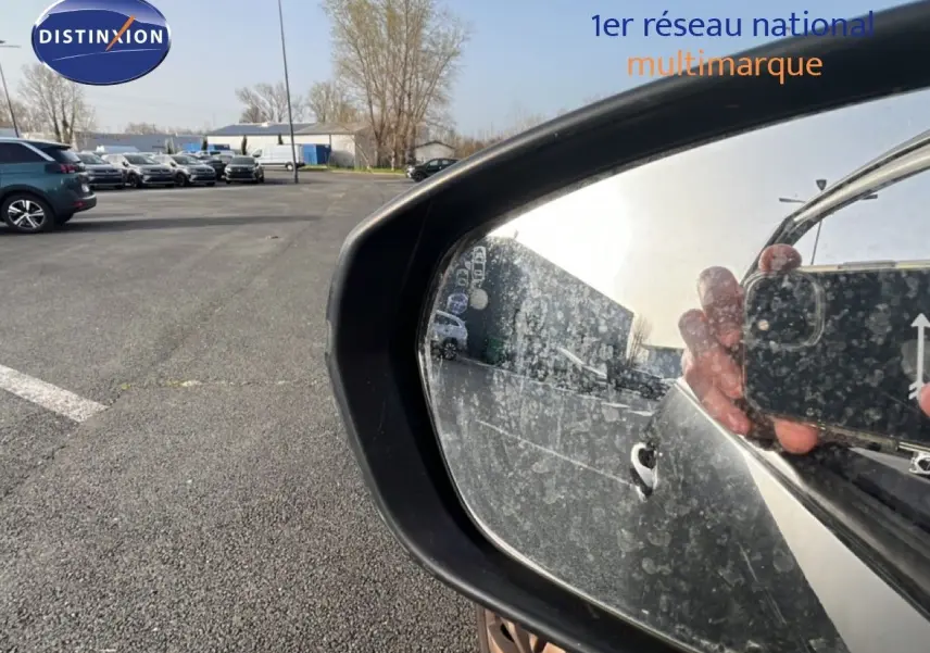 Rétroviseur latéral droit noir perla nera d’un Peugeot 5008 2018, reflet partiel du véhicule et main tenant un smartphone.