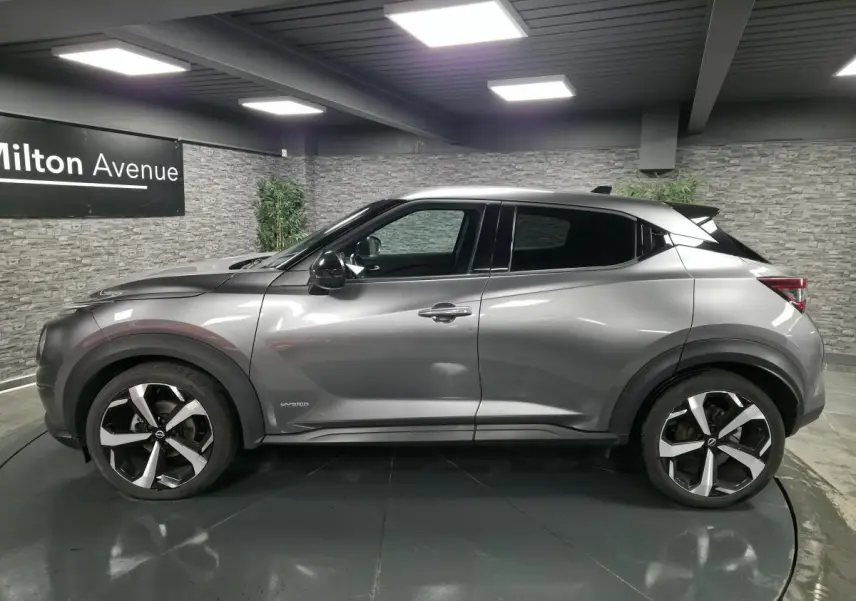Vue latérale droite d'un Nissan Juke gris métallisé 2024 avec jantes alliage noires et grises, badge Hybrid visible.