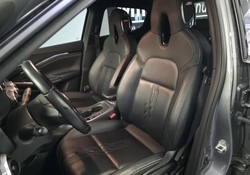 Vue intérieure côté conducteur du Nissan Juke 1.6 Hybrid 2024 avec sellerie cuir noire et accoudoir central.
