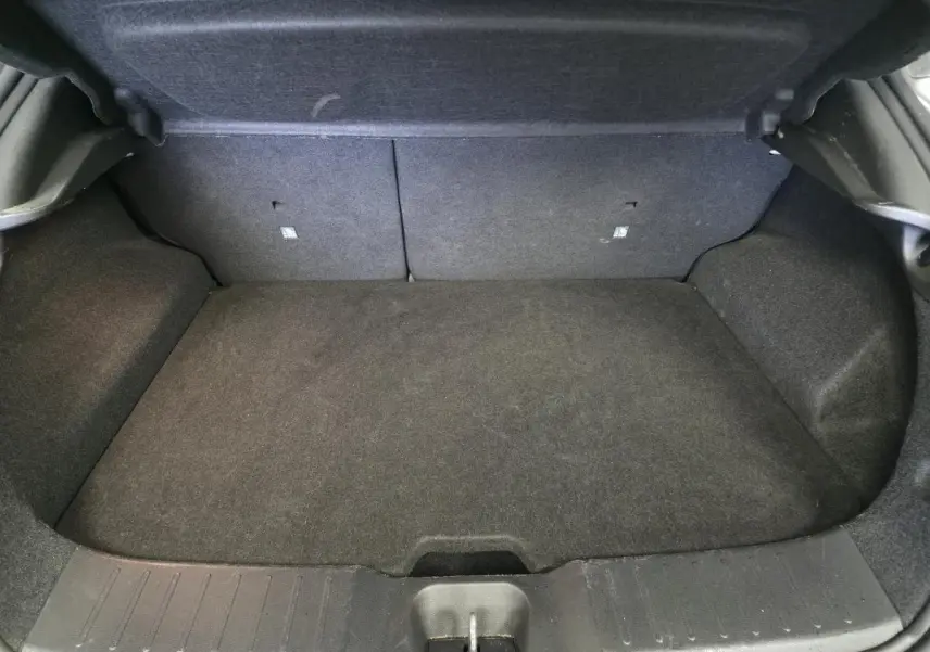 Coffre vide en vue plongeante du Nissan Juke 1.6 Hybrid gris, montrant le tapis et les parois intérieures noires.