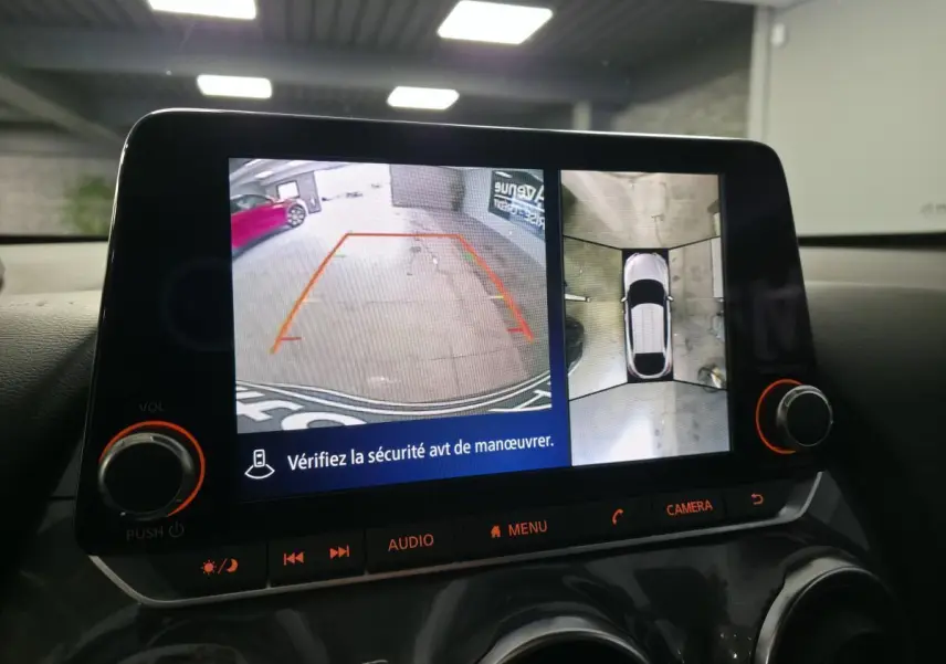 Écran multimédia affichant la caméra de recul et la vue à 360° du Nissan Juke gris en stationnement intérieur.