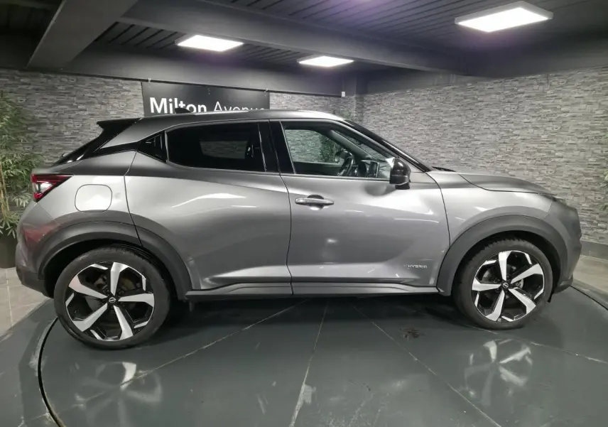 Vue de profil côté gauche du Nissan Juke 1.6 Hybrid gris métallisé avec jantes alliage 19 pouces et badge Hybrid.