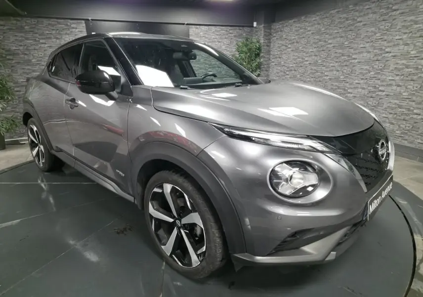 Nissan Juke gris métallisé en 3/4 avant droit, avec jantes alliage noires et toit noir contrasté.
